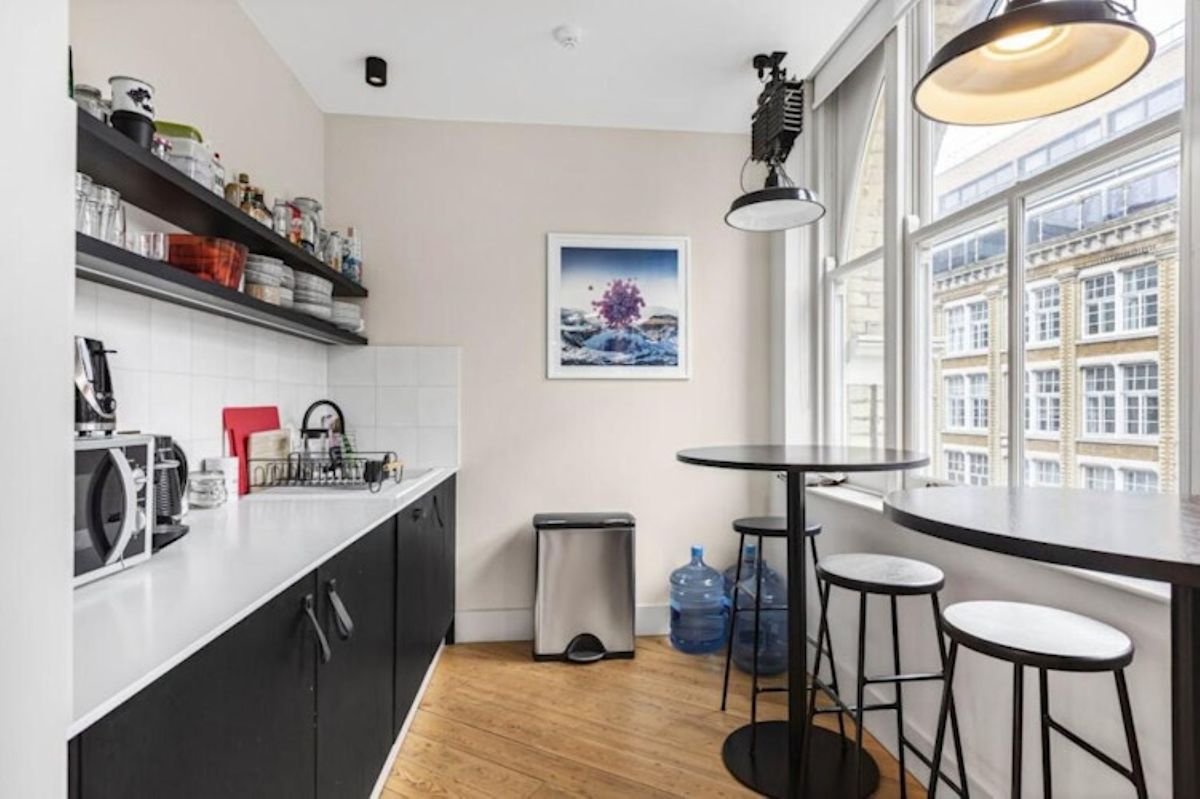 A small kitchen area with shelves, a counter, and a round high table with stools near large windows.