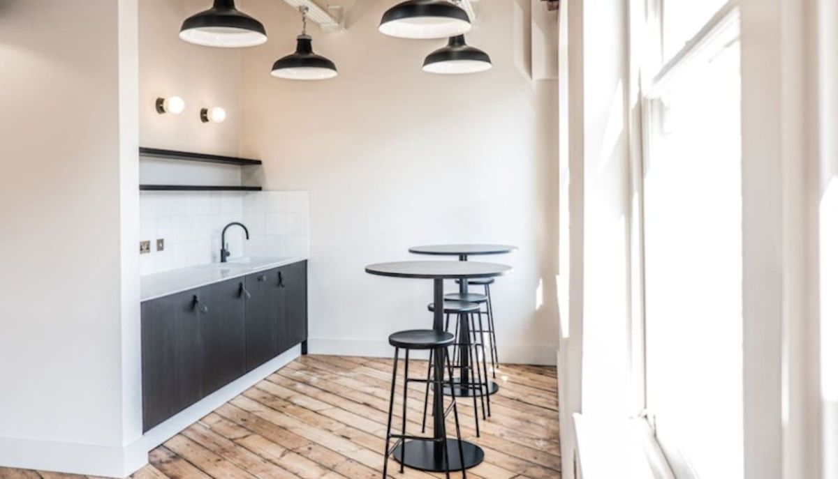 A modern kitchenette with black cabinets and tall bar tables on a wooden floor.