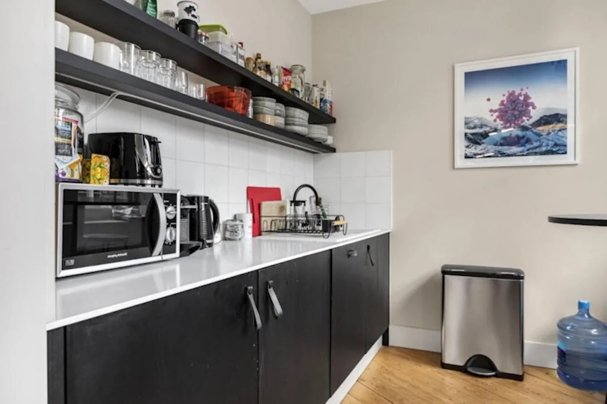 A modern kitchen corner featuring black cabinetry, a countertop with appliances, and a framed artwork on the wall.