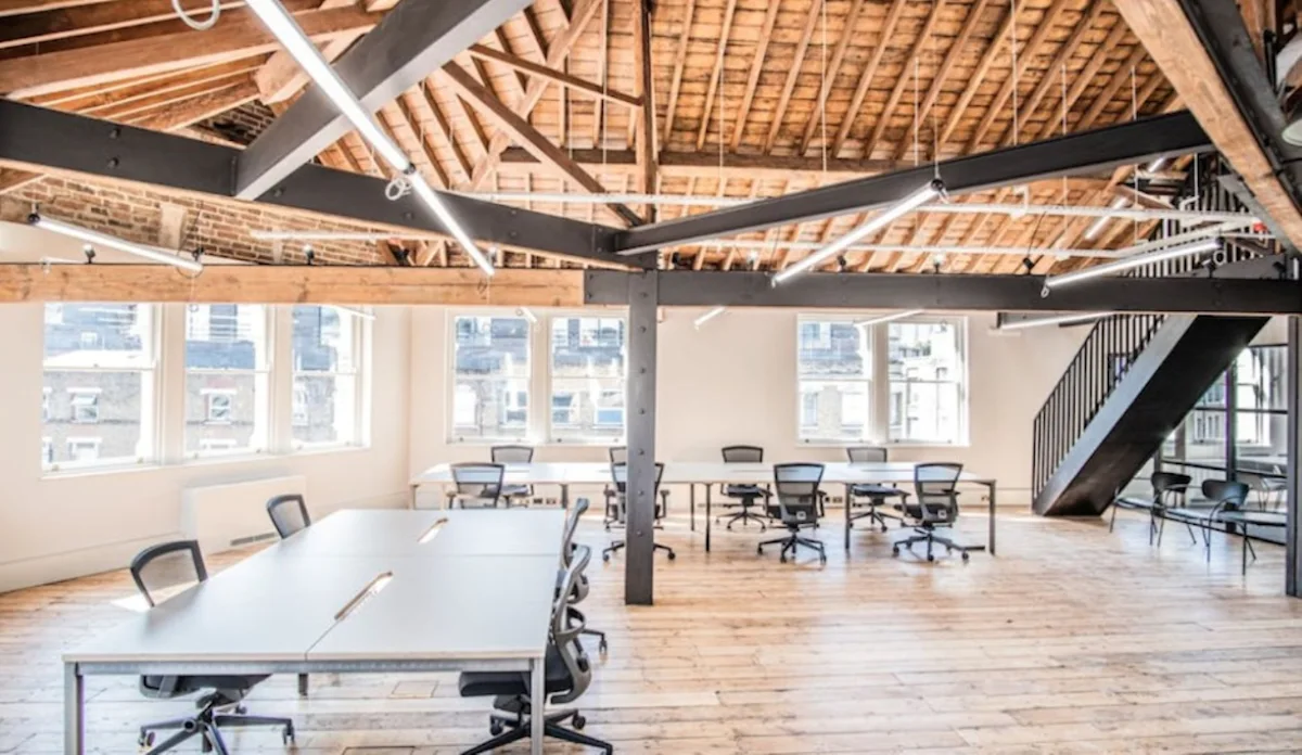 A spacious, modern office interior with exposed wooden beams and several desks and chairs.