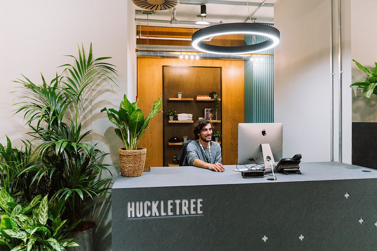 A receptionist sits at the HuckleTree front desk surrounded by plants at Ingestre Place, London.