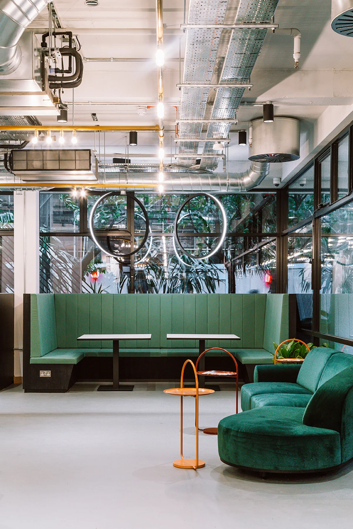 A modern lounge area in Ingestre Place, London, featuring green seating, circular pendant lights, and exposed ductwork.