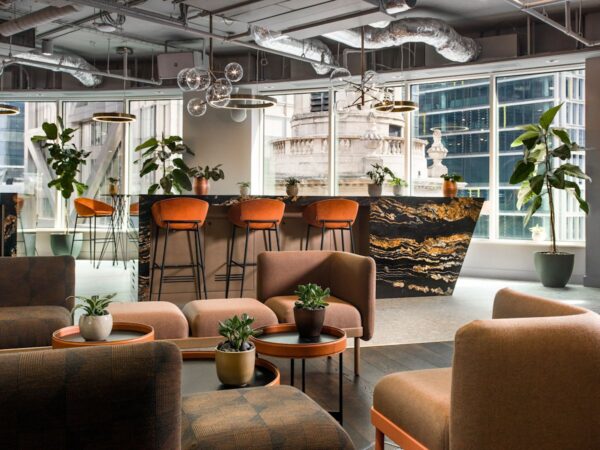 Modern office lounge with elegant seating, lush plants, and a marbled bar counter at Liverpool Street in London.