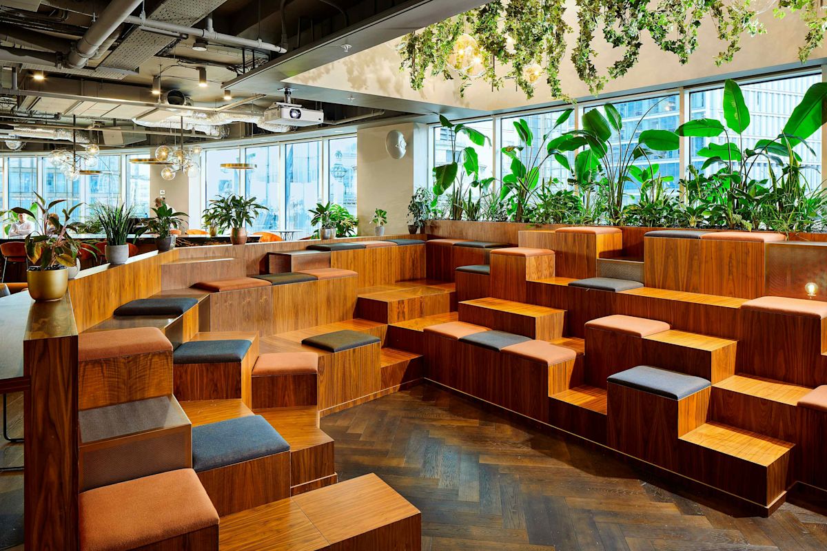 Modern office space with tiered wooden seating and abundant greenery.