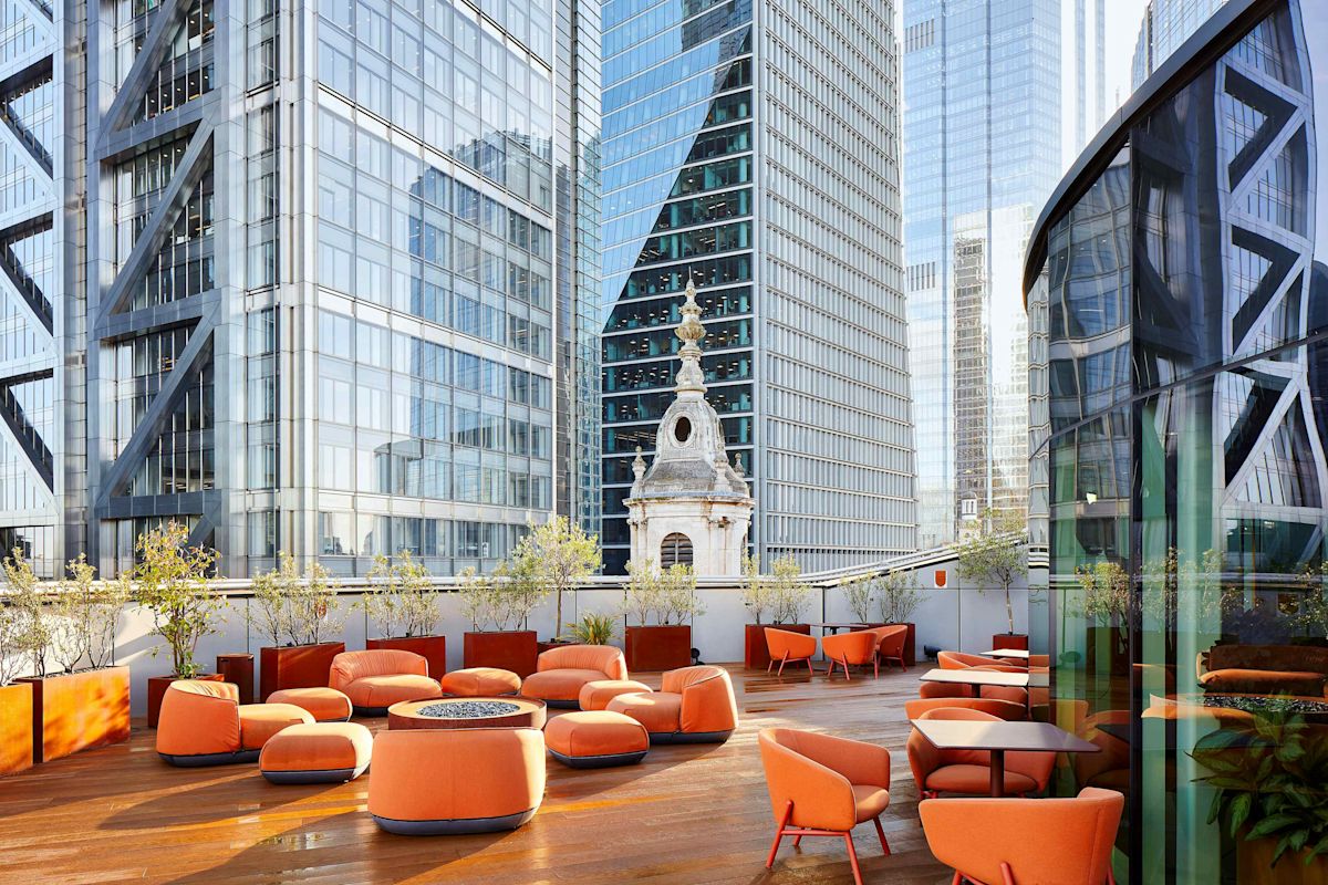 A modern rooftop terrace with orange seating and a view of skyscrapers at Liverpool Street, London.