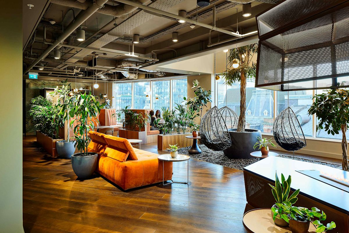 A modern, plant-filled seating area with orange couches and hanging chairs in an office space at Liverpool Street, London.