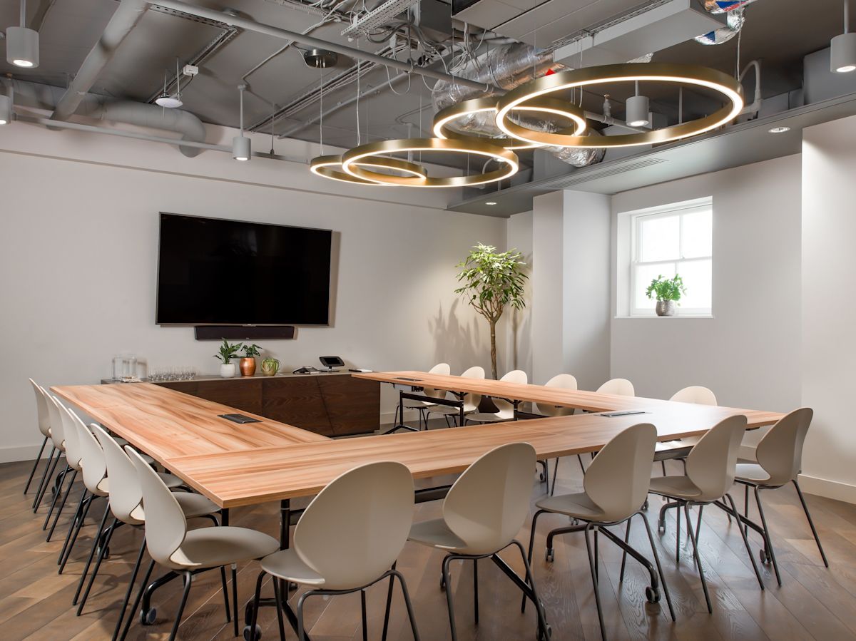A modern conference room with a large wooden table, stylish chairs, and circular ceiling lights.