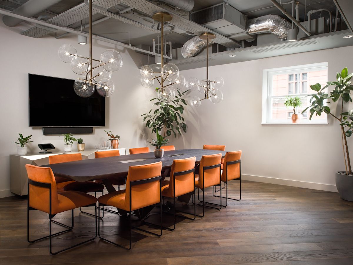 A modern conference room in London with orange chairs, a large table, decorative plants, and stylish lighting fixtures.