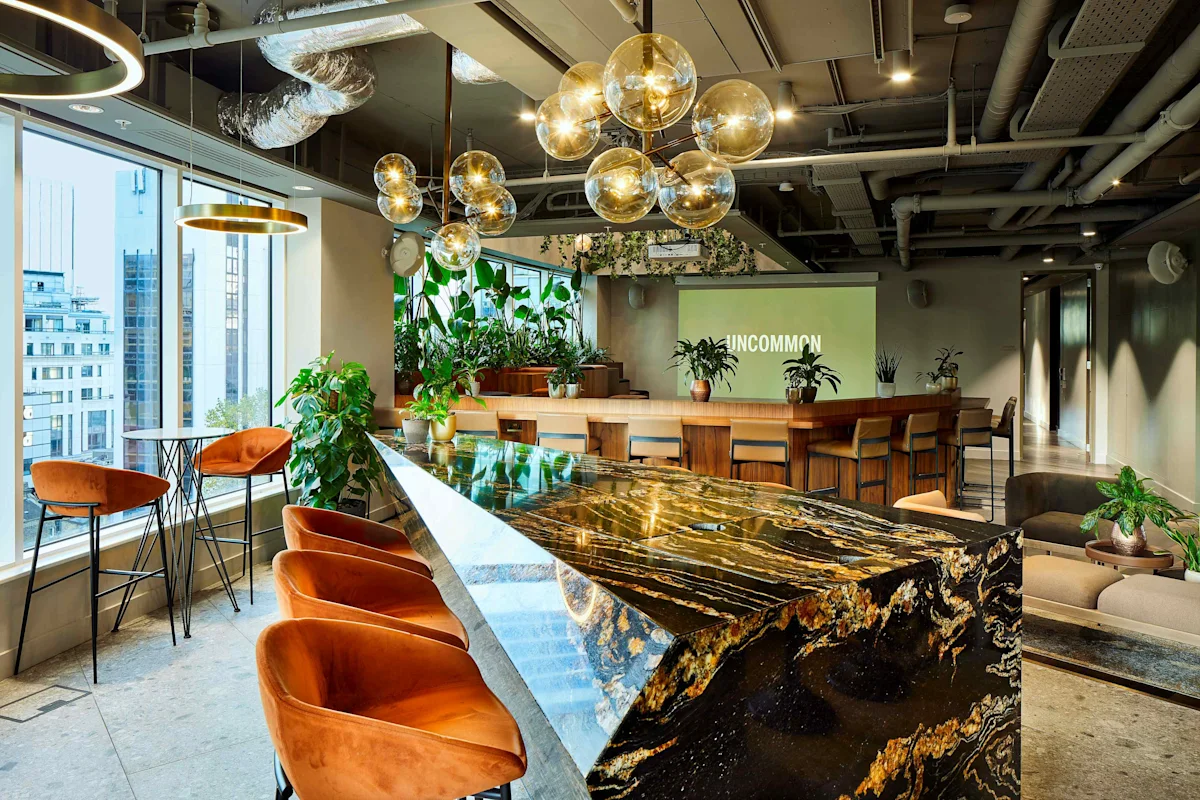 A modern coworking space in Liverpool Street, London, featuring a stylish marble table, orange chairs, and hanging pendant lights.