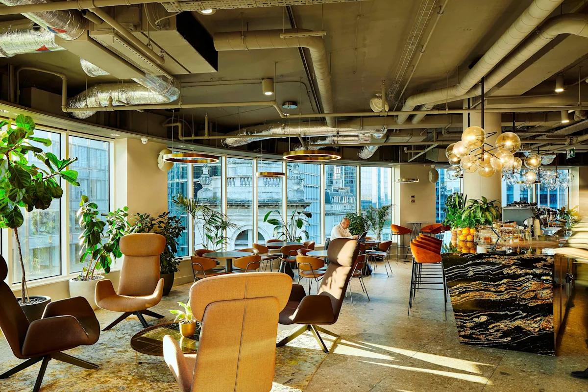 A modern, stylish office lounge area with large windows, plants, and comfortable seating on Liverpool Street in London.