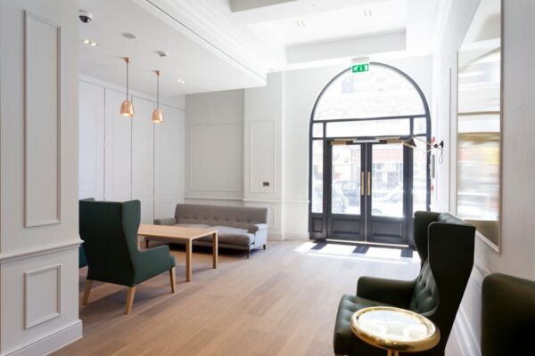A modern waiting area with green chairs, grey sofa, and large arched windows at Liverpool Street 50, London.