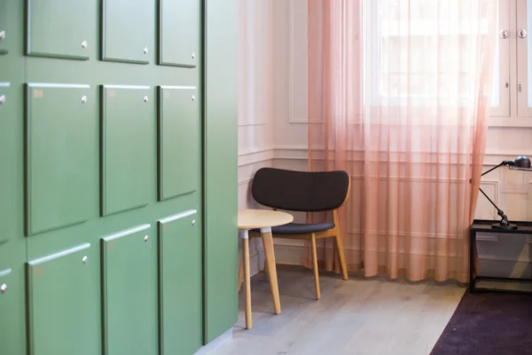 A cozy corner with green lockers, a chair, and a lamp next to light pink curtains.