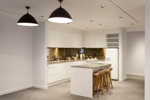 A modern kitchen with white cabinets, an island with stools, pendant lights, and a retro-style fridge.