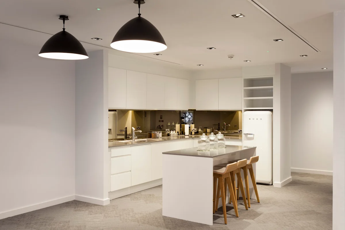 A modern kitchen with white cabinets, an island with stools, pendant lights, and a retro-style fridge.