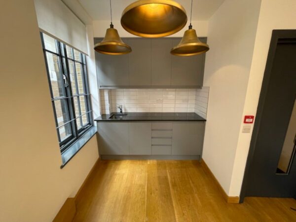 A modern kitchen corner with gray cabinets, wooden floor, and three hanging brass lights at Luke Street 78a, London.
