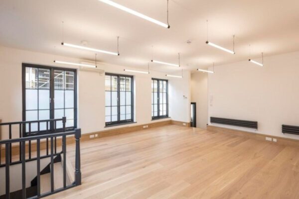 A spacious, empty room with wooden flooring and large windows at Luke Street 78a, London.