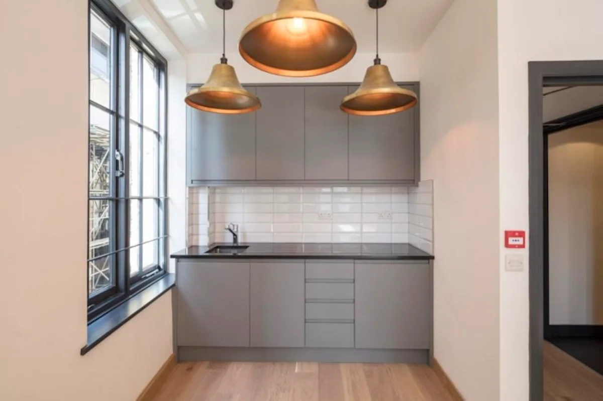Modern kitchen interior with grey cabinets, pendant lights, and tiled backsplash.