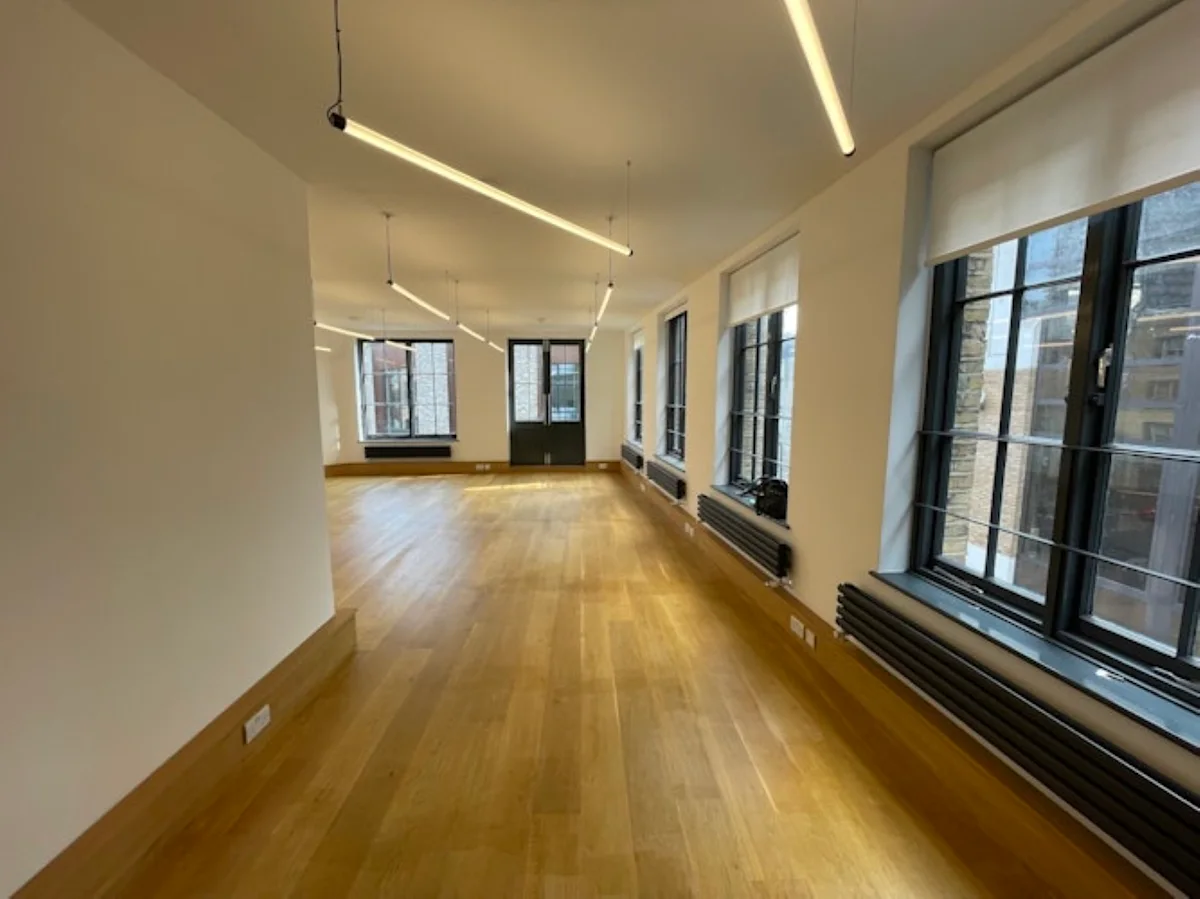 An empty office space with wooden floors and large windows at Luke Street 78a, London.