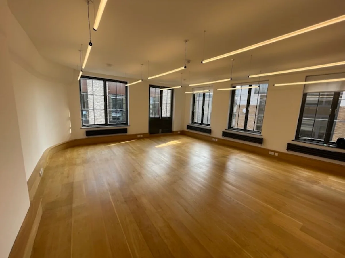 A spacious, empty office room in Luke Street 78a, London, with wooden floors and large windows.