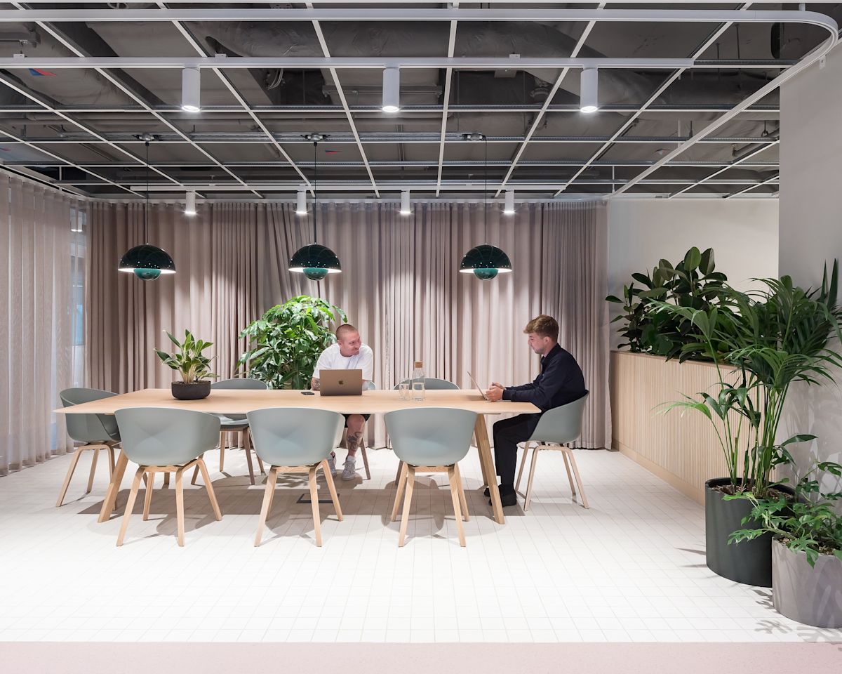 A modern office space at Marsh Wall 77, London, featuring two people working at a table surrounded by plants.