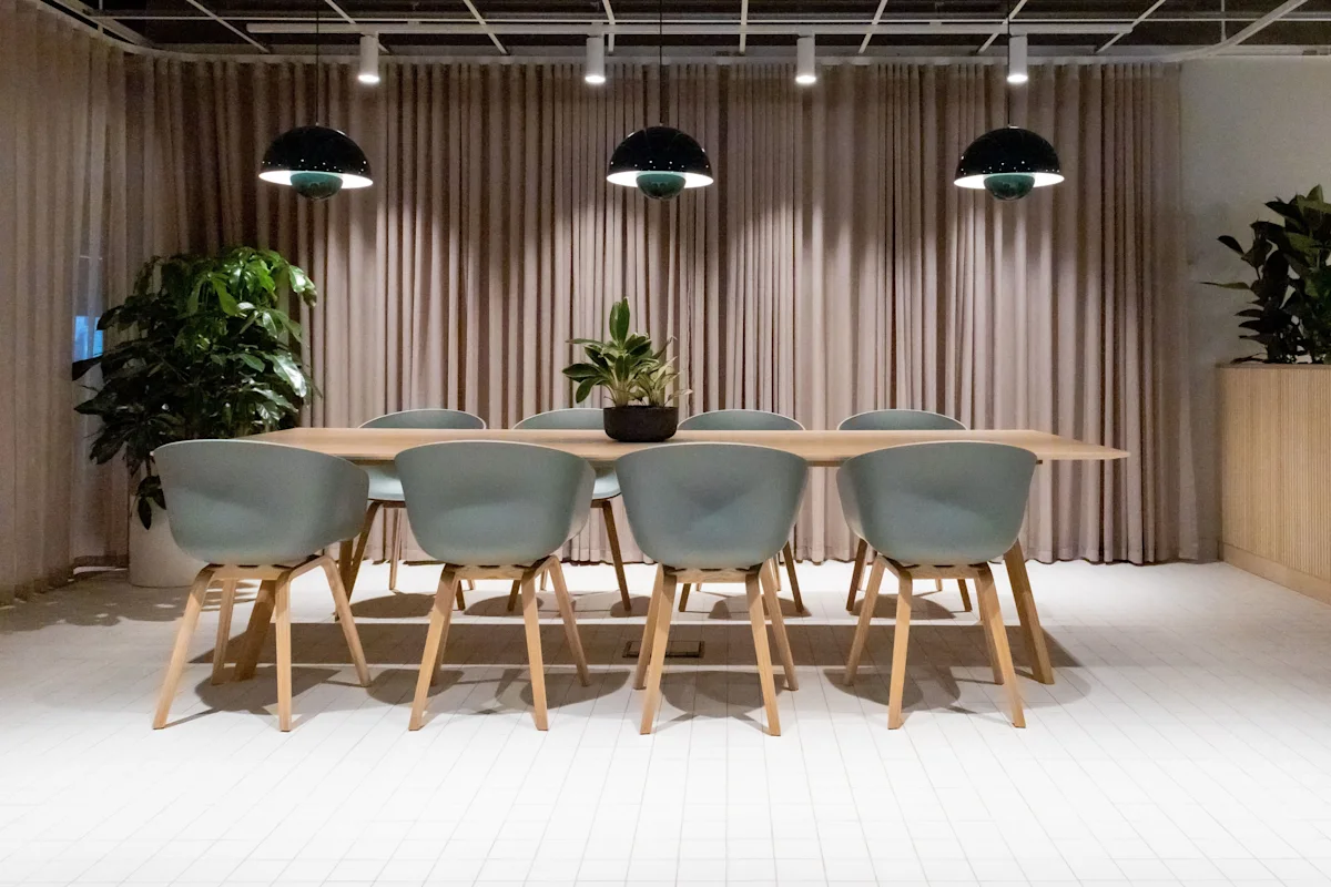 A modern meeting room at Marsh Wall 77 London with a wooden table, blue chairs, and large plants in the background.
