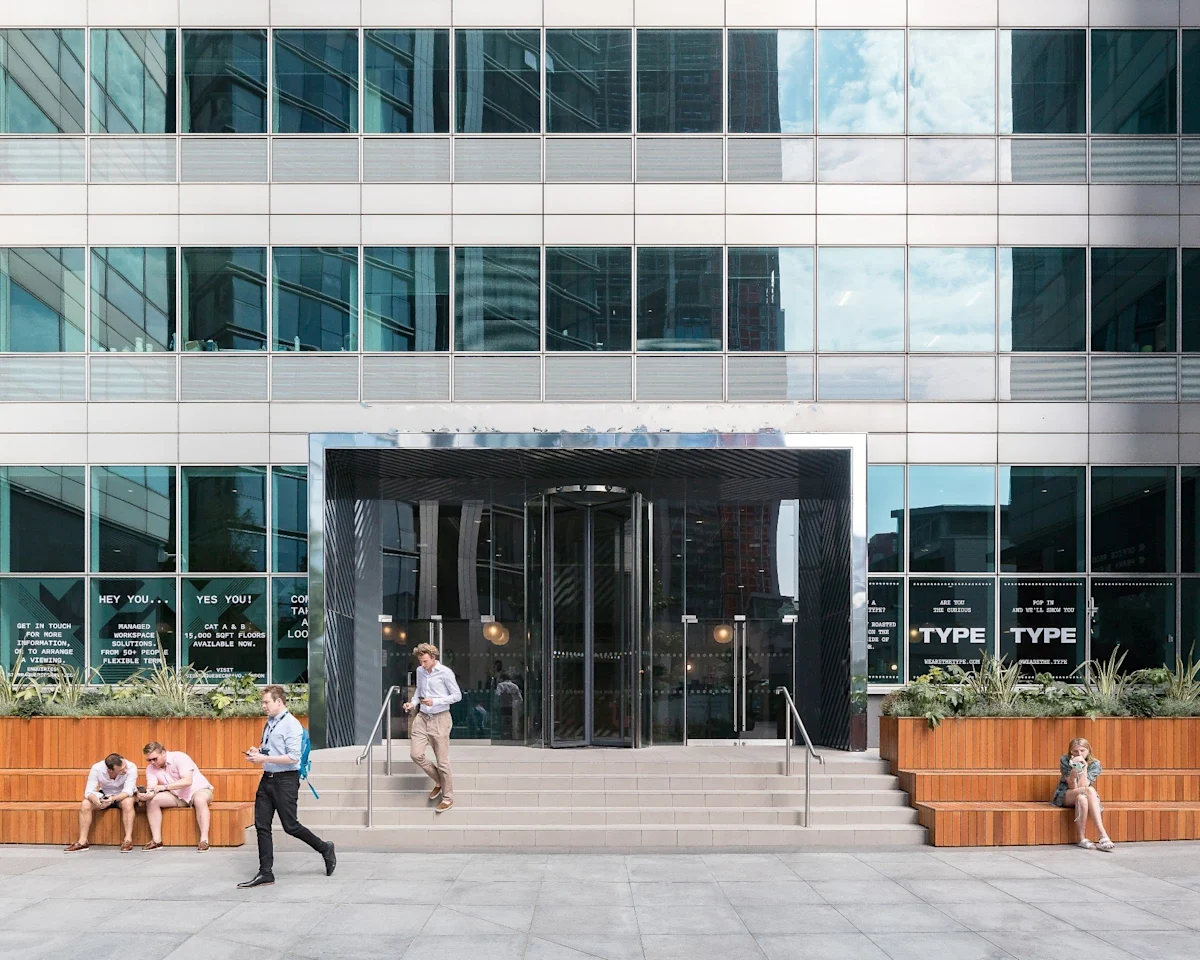 The entrance to 77 Marsh Wall in London with people sitting and walking outside.