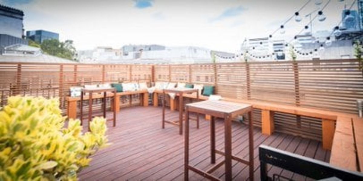 Rooftop terrace with wooden furniture and decorative lights at 46 New Broad Street, London.