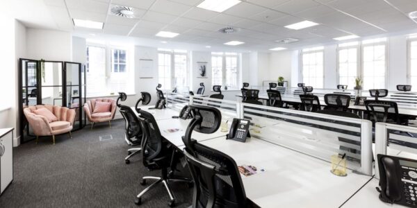 A modern, well-lit office space with multiple workstations, black chairs, and a small seating area with pink chairs.