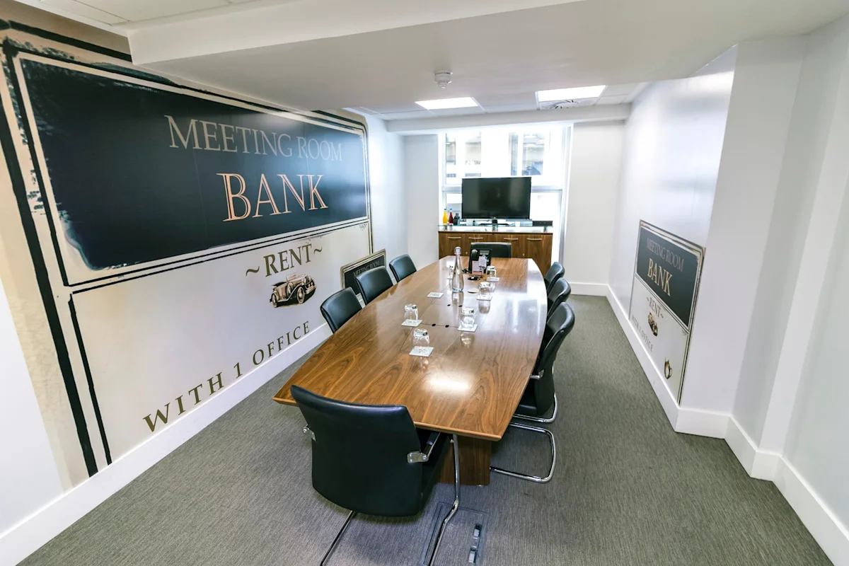 A modern meeting room with a long wooden table and black chairs, located at New Broad Street 46, London.