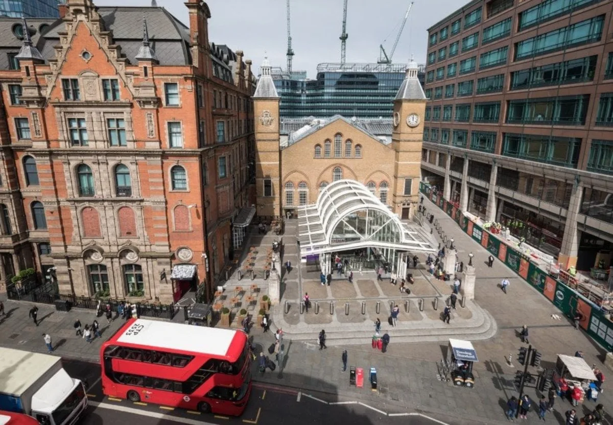 Aerial view of a historic building with a glass entrance and nearby red double-decker bus in New Street, London.