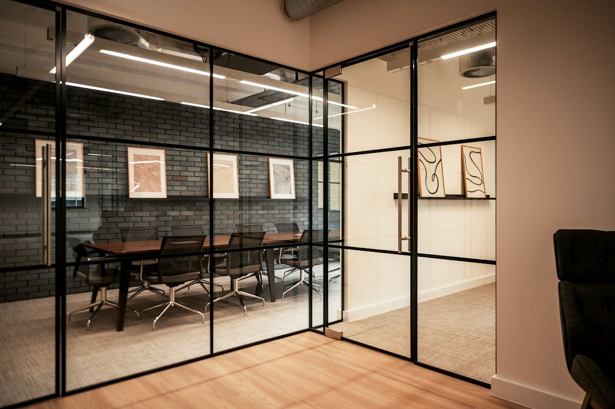 Modern conference room with glass walls and framed artwork on a brick wall.