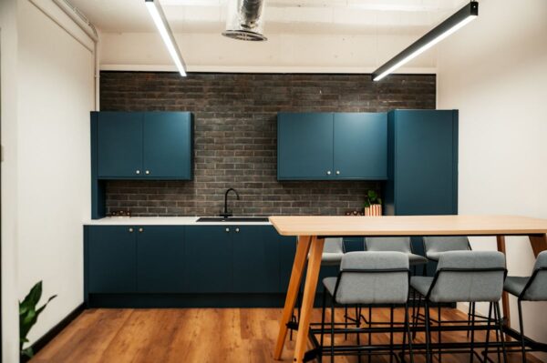 Modern kitchen interior with blue cabinets, a brick wall, and a wooden dining table with chairs.