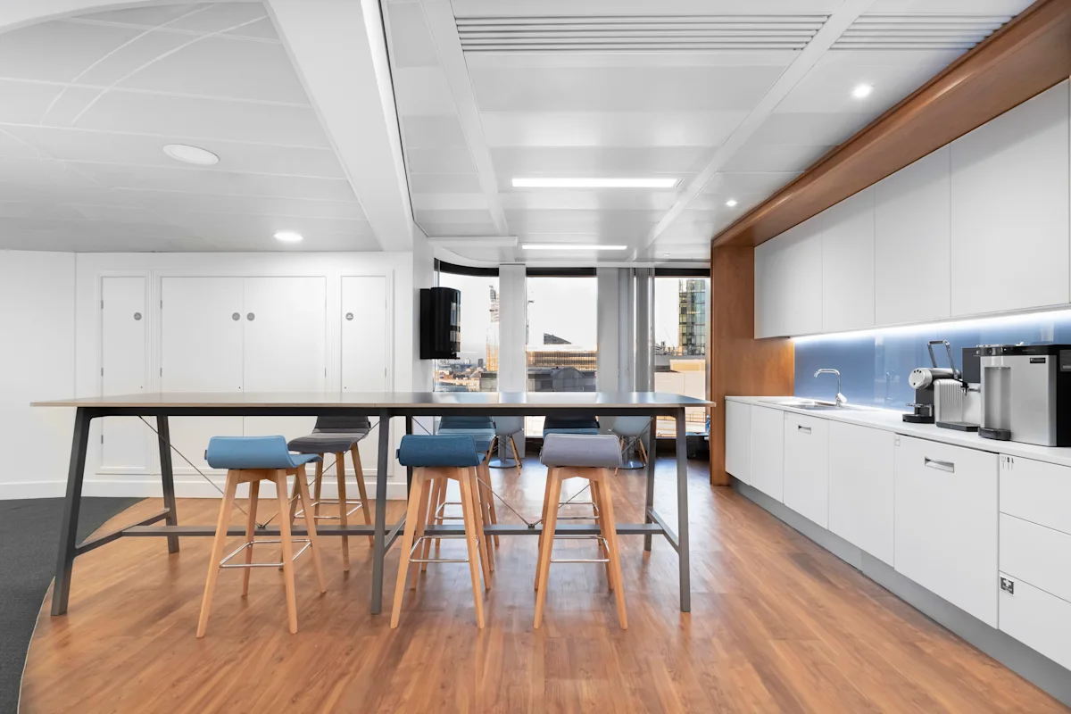 A modern office kitchen with a high table and stools, located in Old Broad Street 25, London.