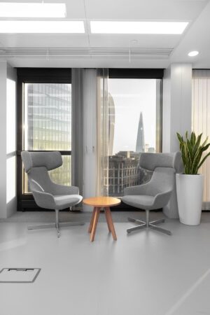 Two modern grey chairs and a small wooden table in an office space with a view of London skyscrapers in the background.