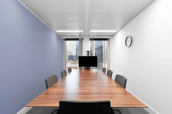 A modern conference room with a wooden table, chairs, a wall clock, and a view of skyscrapers.