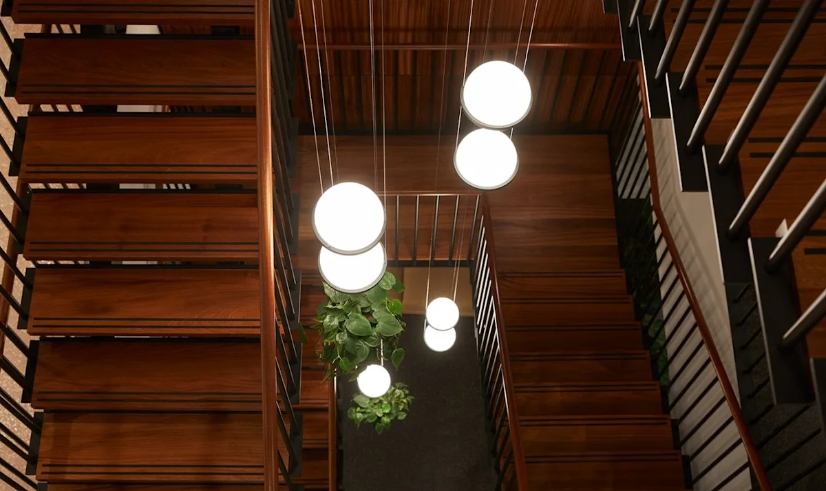 A view down a wooden spiral staircase illuminated by globe pendant lights, with a hanging plant in the center.