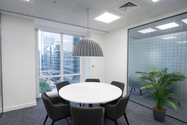 A modern office meeting room with a round table, several chairs, and a large window overlooking city buildings.