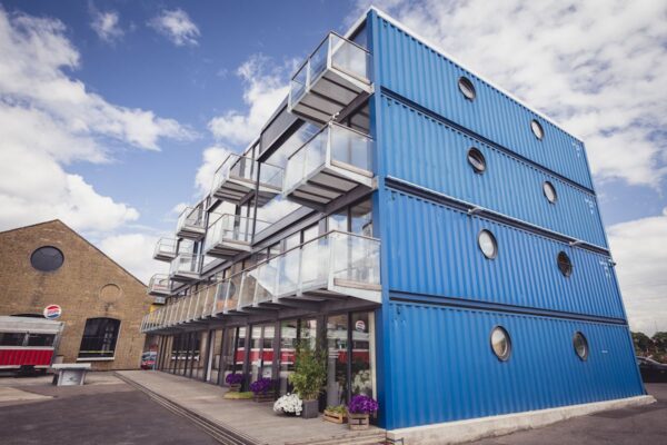 A modern building constructed from bright blue shipping containers with balconies, located in Orchard Place, London.