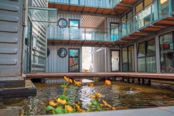 View of modern architecture at Orchard Place 64, London, featuring metal structures and a small pond.