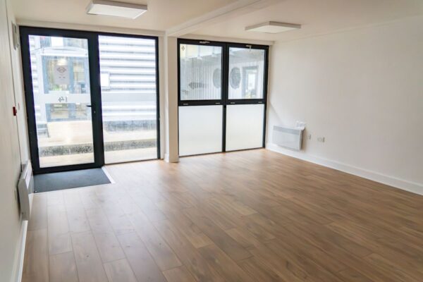 An empty room with wooden flooring and large glass doors at Orchard Place 64, London.