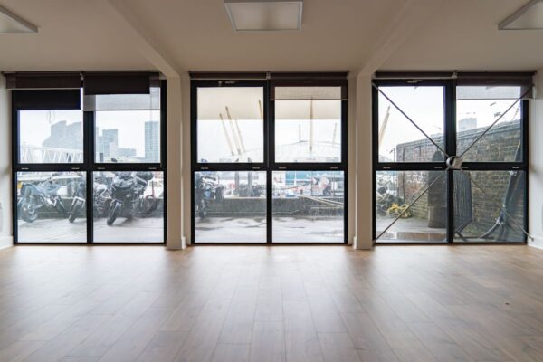 View through large windows overlooking Orchard Place 64 in London, featuring parked motorcycles and the O2 Arena in the background.