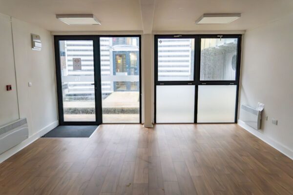 An empty room with wooden flooring and large glass doors in Orchard Place 64, London.