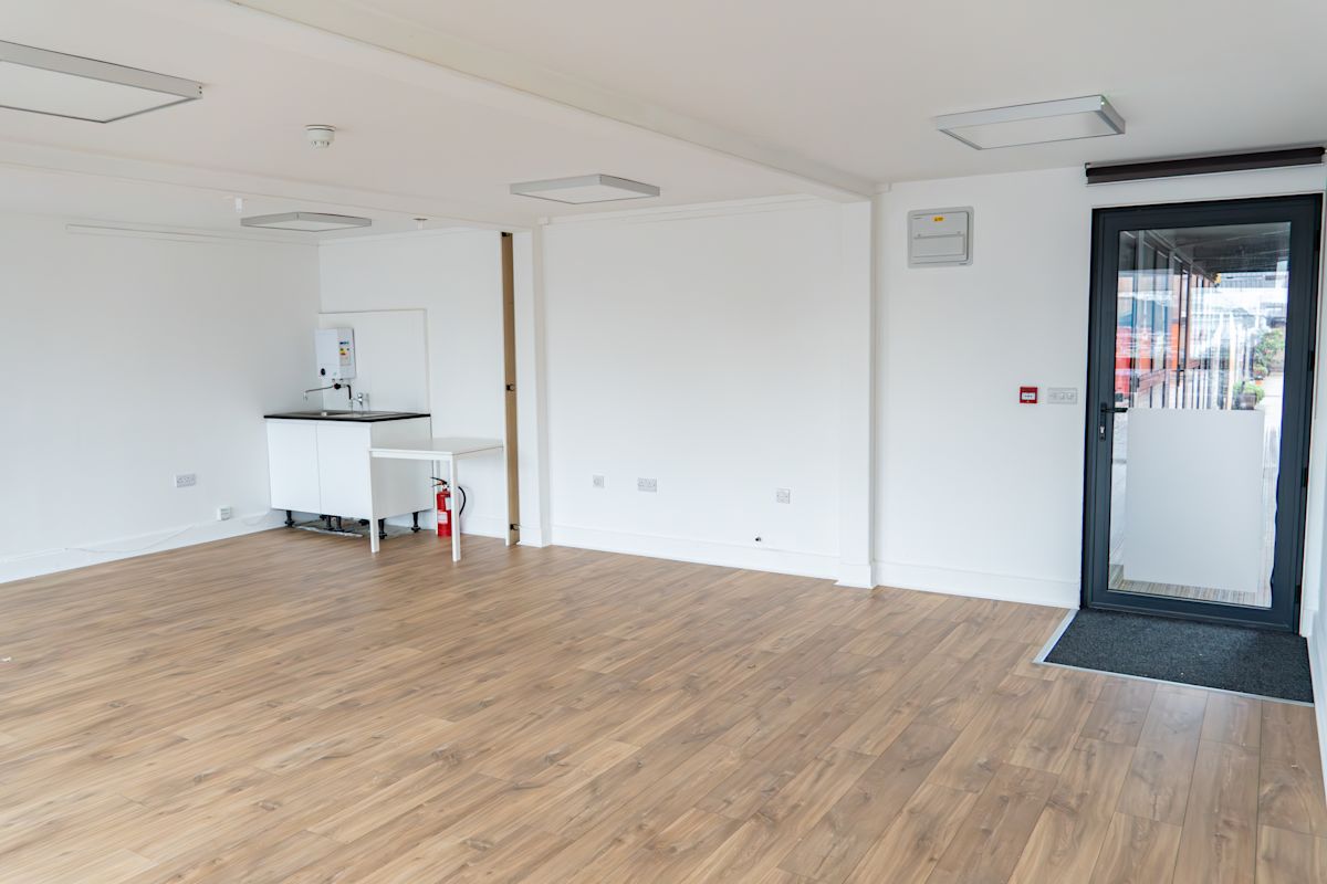 An empty room with wooden flooring, a small kitchenette, and a glass door at Orchard Place 64 London.