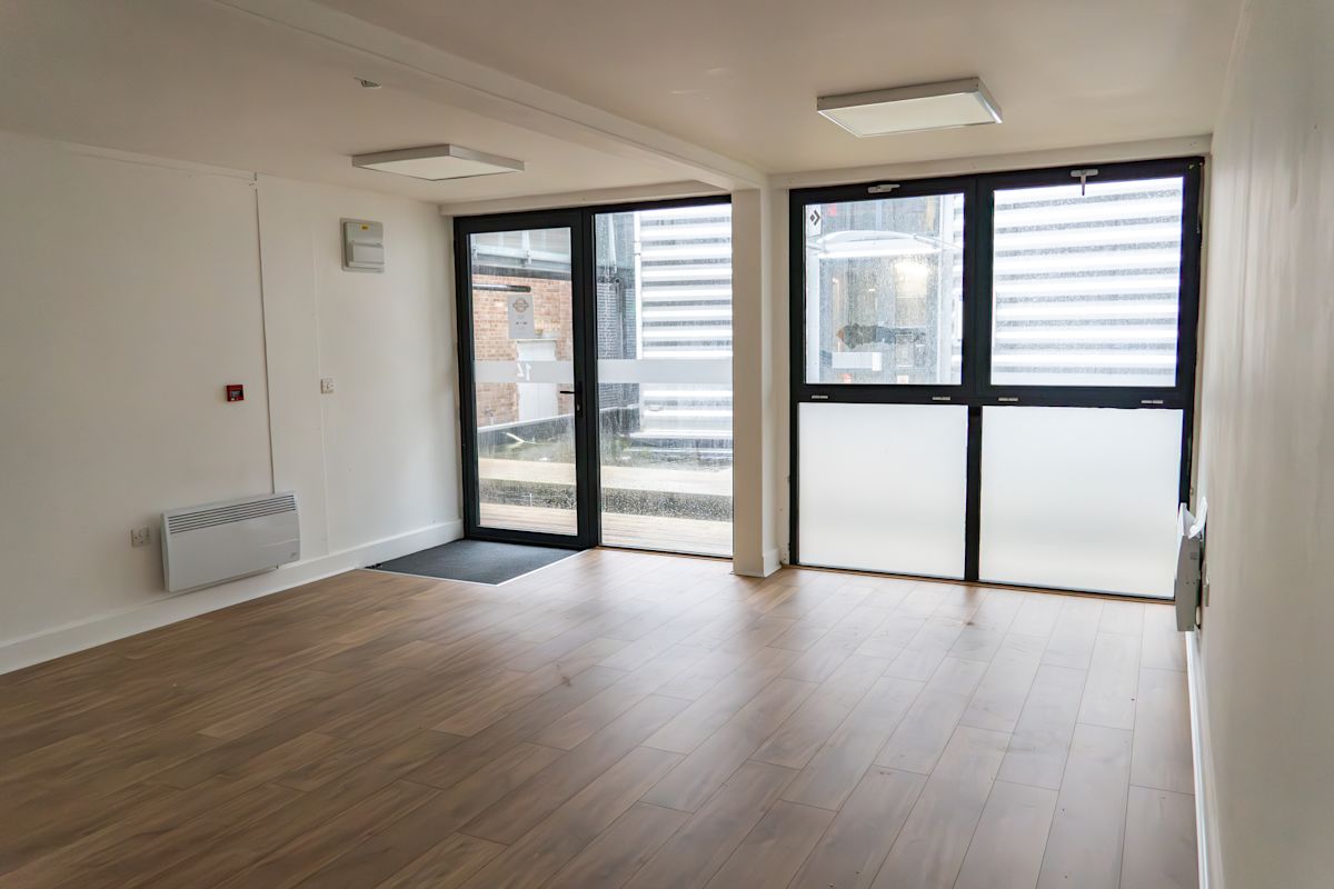 Empty room with wooden flooring and large windows at Orchard Place 64, London.