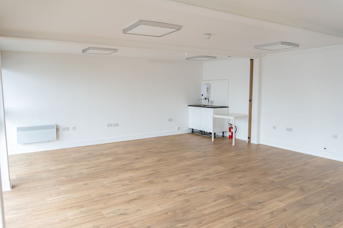 An empty room with wooden flooring and a small kitchenette in Orchard Place 64, London.