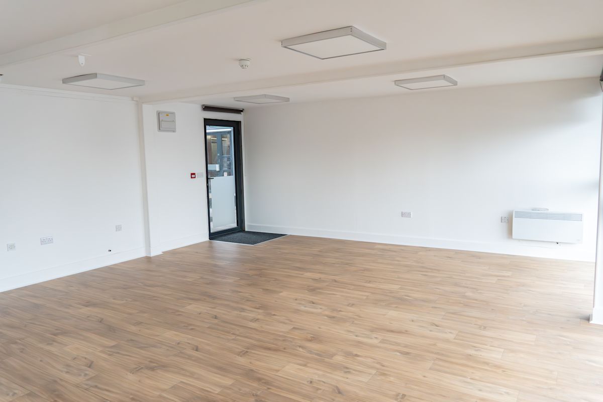 An empty, bright room with wooden flooring and a glass door.
