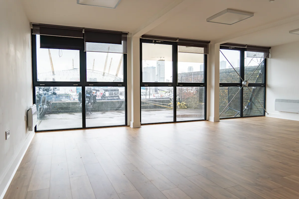 An empty room with large floor-to-ceiling windows overlooking an urban landscape in London at Orchard Place 64.