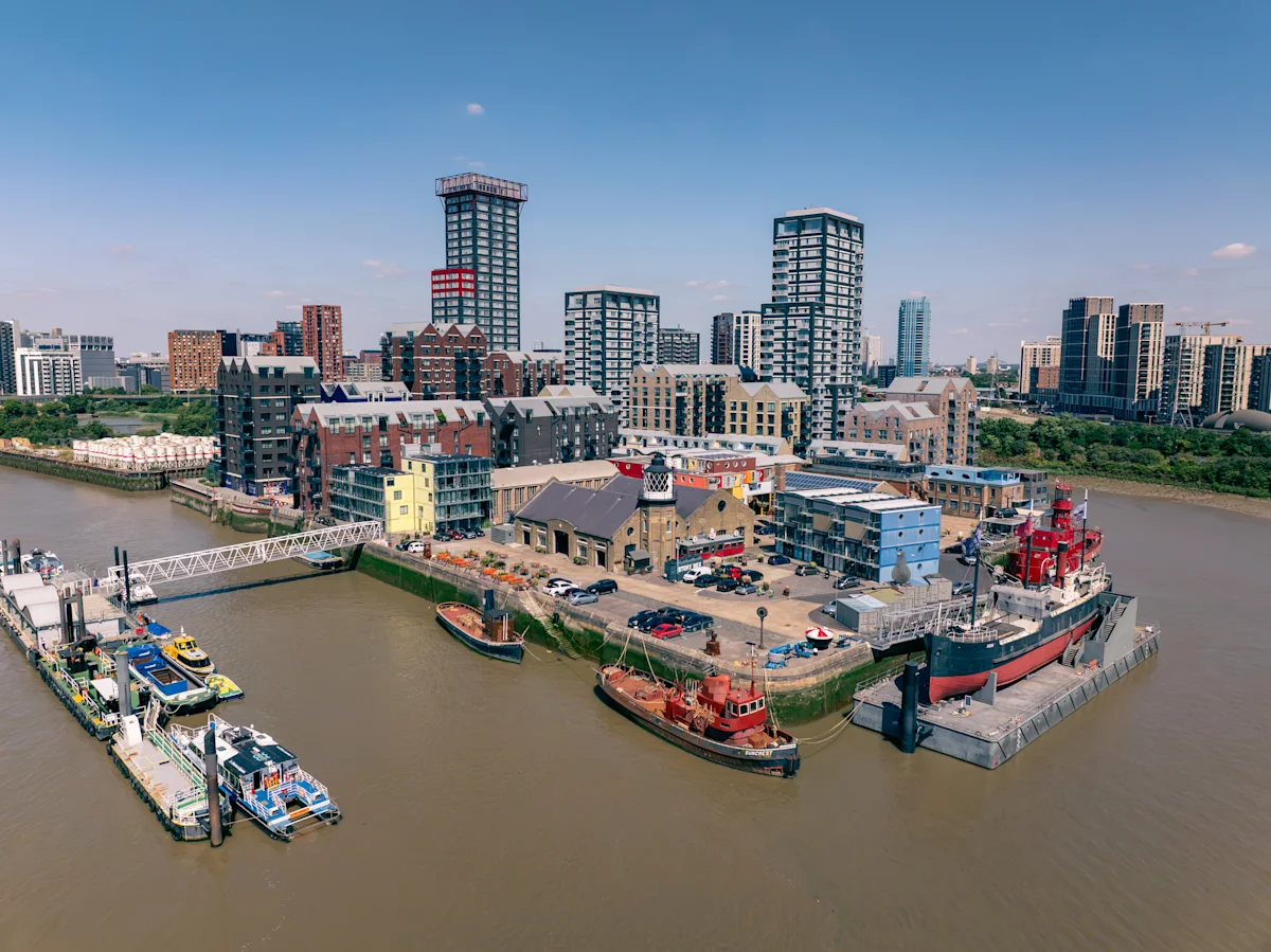 Aerial view of Orchard Place 64 in London, featuring a riverside development with modern buildings and moored boats.