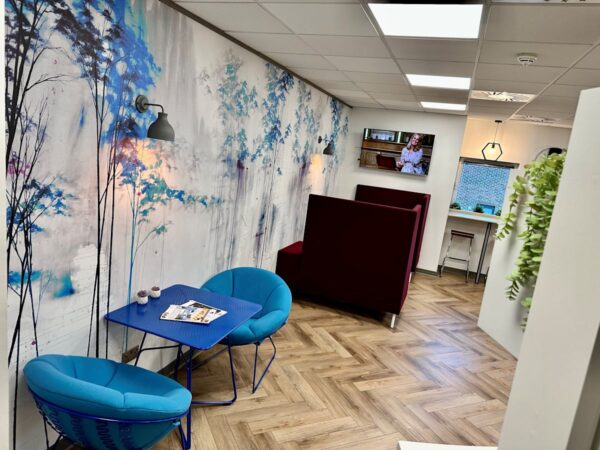 A modern office lounge area with blue chairs, a scenic mural, and a wall-mounted television.