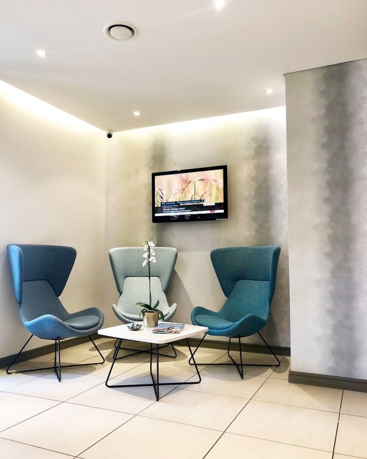 Modern waiting area with three blue chairs, a small table, and a wall-mounted TV.